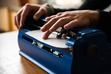 Crop anonymous visually impaired male typing on typewriter with tactile writing system  at home