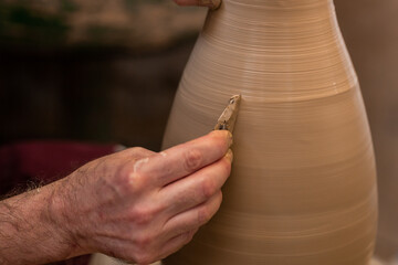Crop unrecognizable sculptor with equipment giving shape while sculpting with brown clay on throwing wheel