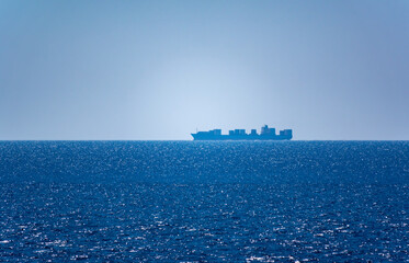 Calm blue sea with the silhouette of a large ship on the horizon