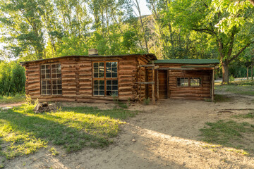 Side view of a log cabin with on bare ground and big green trees all around, double hung grid windows and panel doors, Josie Bassett Morris log cabin, Dinosaur National Monument, Utah