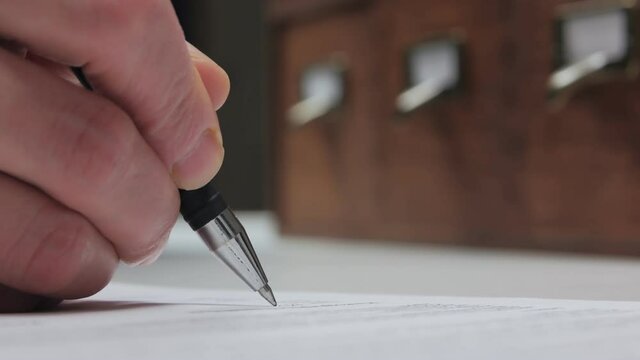 Close-up of a woman's hand filling out documents, a passport lying on the table next to it.