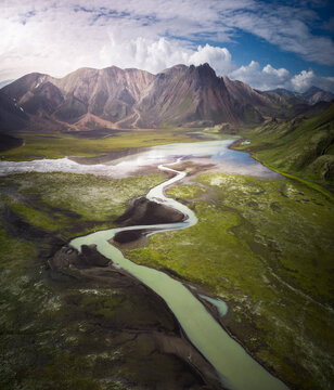 Amazing view of curvy blue river loop streaming on rough hilly terrain covered with lush abundant vegetation in Iceland