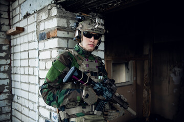 Military man with assault rifle standing inside building, he is ready for combat