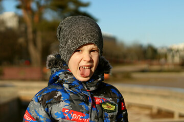 Fototapeta na wymiar Little boy shows tongue to camera in park close-up