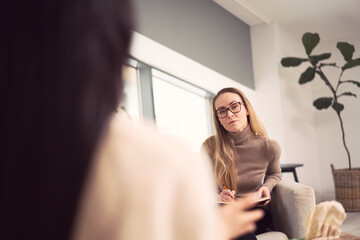 Female counselor sitting in armchair and giving advice to unrecognizable client during psychotherapy appointment
