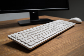 White modern keyboard and mouse near computer placed on wooden table