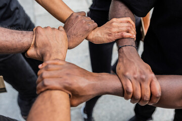 From above of crop anonymous African American partners holding hands demonstrating unity symbol in town