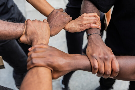 From above of crop anonymous African American partners holding hands demonstrating unity symbol in town