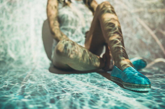 Anonymous female in summer shoes sitting under abstract projection of tangled white lines