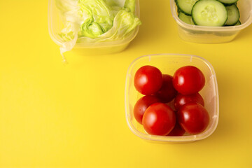 Containers with fresh vegetables on a yellow background