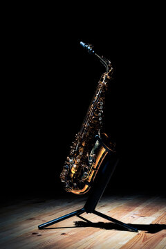 Shiny golden tenor saxophone on stand placed on wooden stage against black background