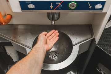 The guy brings his hand to the automatic water supply tap in the modern toilet of the stadler electric train
