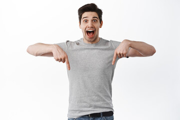 Happy handsome guy rejoicing, scream from joy and pointing fingers down, showing promo offer on...