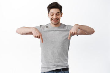 Advertising. Smiling adult man pointing and looking down with happy pleased face, found something cool, showing promo, standing over white background