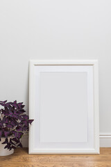 Vertical mockup of white classic photo frame standing on the wooden floor