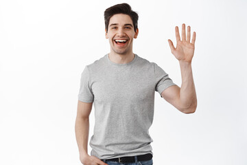 Hello. Friendly handsome man waving at you, welcoming gesture, saying hi and greeting, meet guests, standing over white background