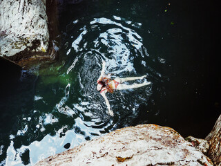 The girl swims with her arms outstretched to the sides in the turquoise river between the rocks. Top view
