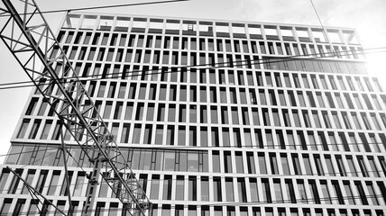 Train railway catenary and pantograph cables and electric wires against modern office building. Black and white.