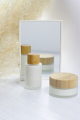 Glass matte cosmetic cream bottles with wooden top, eco cosmetics and mirror on white, lotion serum face body treatment