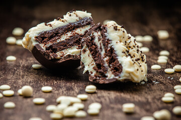 Stuffed chocolate easter egg with white chocolate on the top and white chocolate callets around on a wooden table. Gourmet.