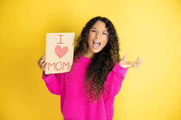 Beautiful woman celebrating mothers day holding poster love mom message crazy and mad shouting and...