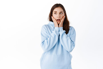 Young shocked girl student drop jaw, gossiping and staring aside at logo, holding hands on cheeks...