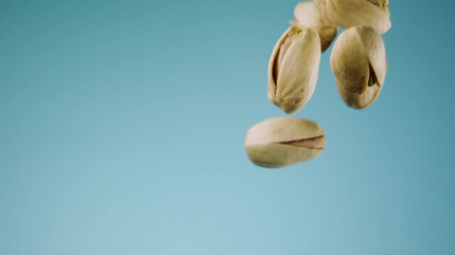 Macro shot in slow motion of pistachio falling over blue background