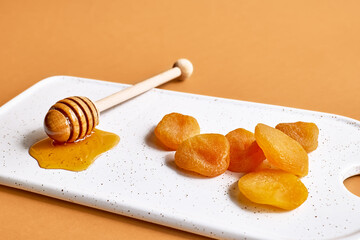 Fototapeta na wymiar Dried apricots and honey in white plate on orange background. Dehydrated fruits. Healthy sweets concept.