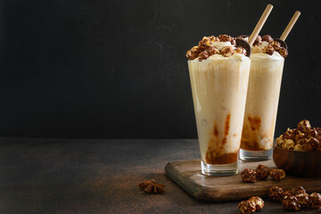 Tasty banana milkshake garnished with caramel, whipped cream, popcorn on dark background. Space for text.