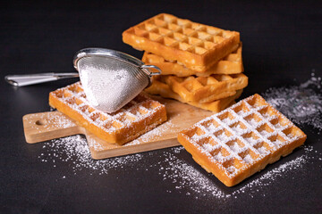 Sweet waffles sprinkled with powdered sugar prepared for serving. A tasty dessert eaten with fruit and preserves.