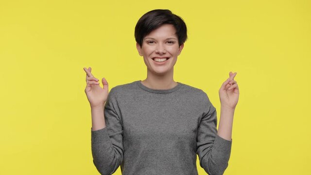 Color of the year 2021. Ultimate Gray and illuminating. Young beautiful woman wearing gray sweatshirt praying for good luck, cross fingers and making a wish isolated on yellow background
