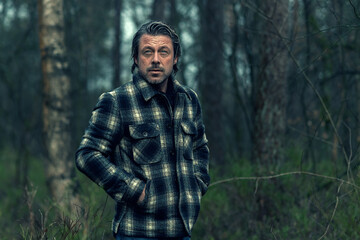 Man with stubble beard in a checkered coat in a rainy forest.