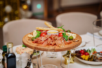 appetizer, cheese meat platter with honey, garnished with fresh basil. the table is set for a birthday or wedding celebration. holiday. restaurant