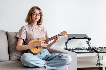 young smiling woman playing ukulele in the apartment