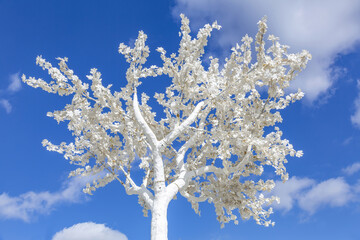 Unusual branches of a white decorative plastic tree against a bright blue cloudy sky