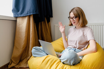 young woman speaking videochat using laptop waving her hand at home