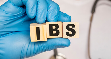 IBS Irritable bowel syndrome - word from wooden blocks with letters holding by a doctor's hands in medical protective gloves. Medical concept.