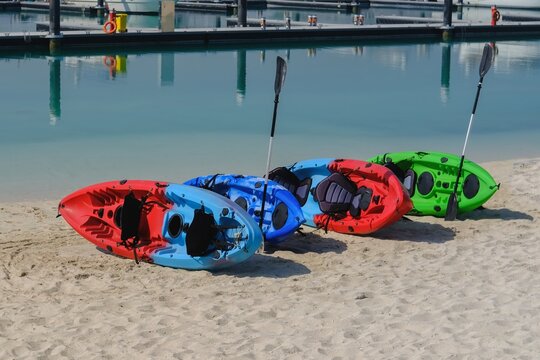Colorful multi colored kayaks lying orderly on sandy beach at sport recreation area.Beach family activities, paddling,kayaking,surfing. Boat for rafting on water. Outdoor sport activities.Watersport.