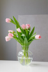 pink tulips with green leaves in a glass vase, a woman holding tulips in her hands, florist, floristry, mother's day gift, bouquet for March 8, bouquet for a girl on her birthday, bouquet of tulips