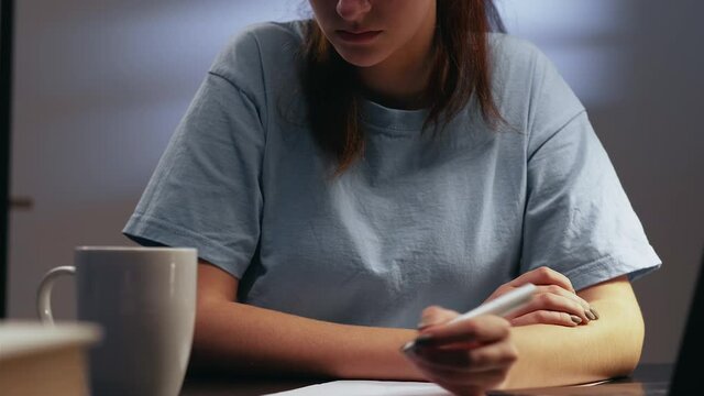 Night study. Home learning. Knowledge education. Confident tired smart left-handed female student busy with task writing essay late at evening workplace with coffee mug on desk.