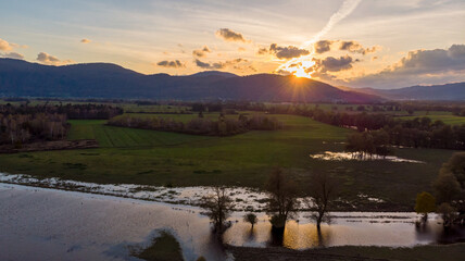 Spectacular aerial panorama of river flowing through fields at sunset.