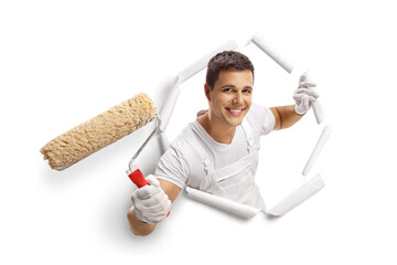 Young male painter with a roller peeking through a paper hole