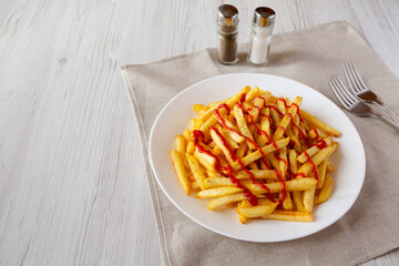 Homemade French Fries with Ketchup, Salt and Pepper on a white plate on a white wooden background, side view. Copy space.
