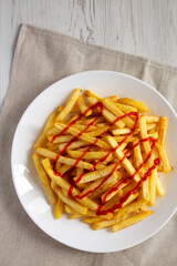 Homemade French Fries with Ketchup, Salt and Pepper on a white plate on a white wooden surface, top view.