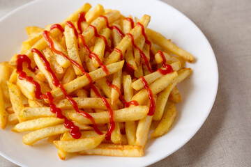 Homemade French Fries with Ketchup, Salt and Pepper on a white plate on a white wooden background, side view. Close-up.