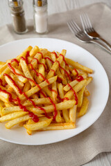 Homemade French Fries with Ketchup, Salt and Pepper on a white plate on a white wooden background, side view. Close-up.