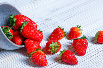Fresh red strawberries sprinkled from a bowl on a white rustic plate. Copy space for text.