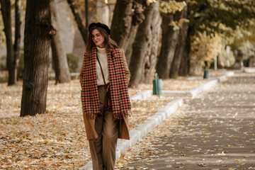 beautiful young woman in beret and coat walks in the autumn city