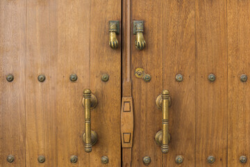 Detail of a studded, wooden door with iron doorknobs and hand knockers