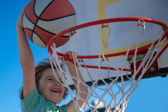 Kid boy basketball player with a ball scoring a goal. Child Player scoring slam dunk, stock photo. Cute smiling boy plays basketball.